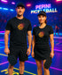 Two people wearing black t-shirts with a colorful design, holding pickleball paddles on a court with 'PEPINI PICKLEBALL' branding.
