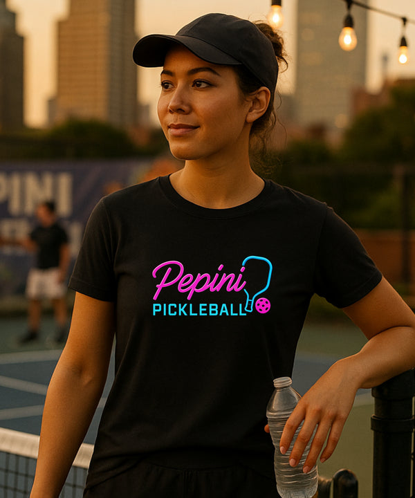 Woman wearing a black t-shirt with 'Pepini Pickleball' logo, holding a water bottle on a pickleball court.