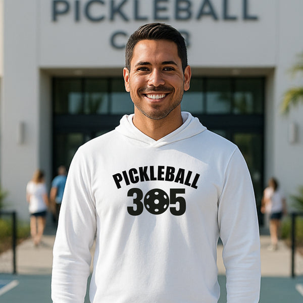 Man wearing a white hoodie with 'Pickleball 305' text, standing in front of a pickleball court building.