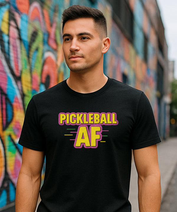 Man wearing a black t-shirt with 'Pickleball AF' text in front of colorful graffiti.