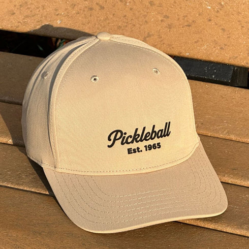 Beige cap with 'Pickleball Est. 1965' text on a wooden surface