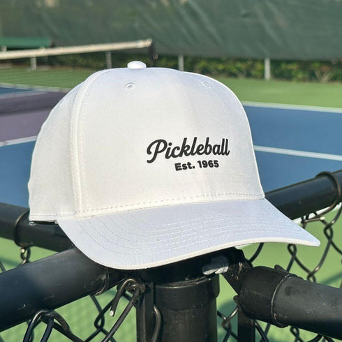 White cap with 'Pickleball Est. 1965' text on a tennis court background