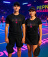 Two people wearing black 'Pickleball' shirts on a pickleball court with colorful lighting.