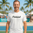 Man wearing a white 'Pickleball' t-shirt on a pickleball court with palm trees in the background.