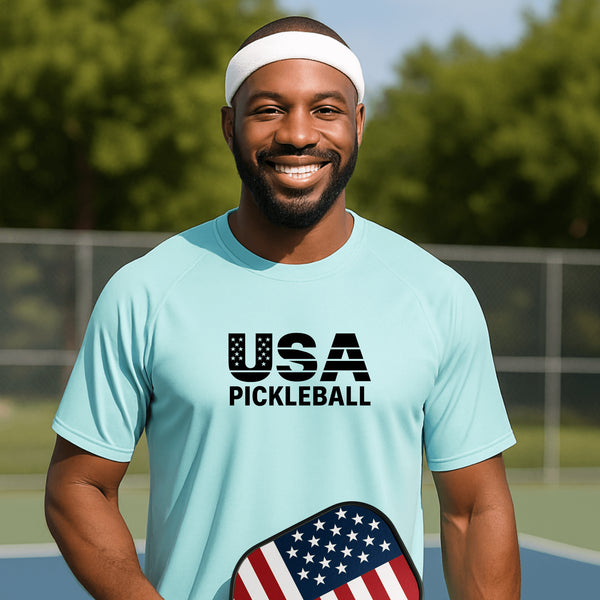Man wearing a light blue 'USA Pickleball' t-shirt on a pickleball court.
