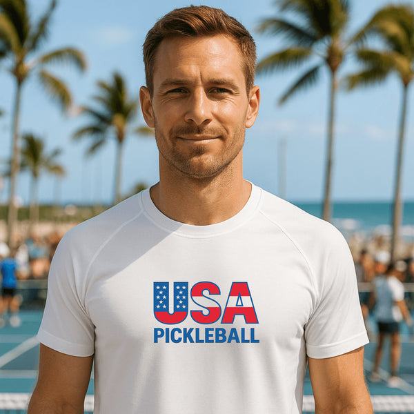 Man wearing a 'USA Pickleball' t-shirt on a pickleball court with palm trees in the background.